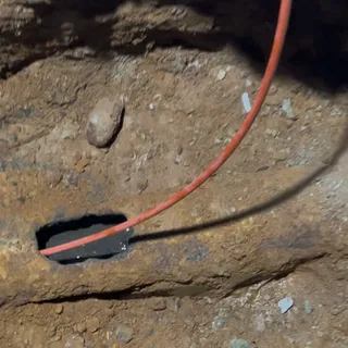 Close-up at the base of an excavation: an orange cable running down the earth face and into a small opening in the existing line